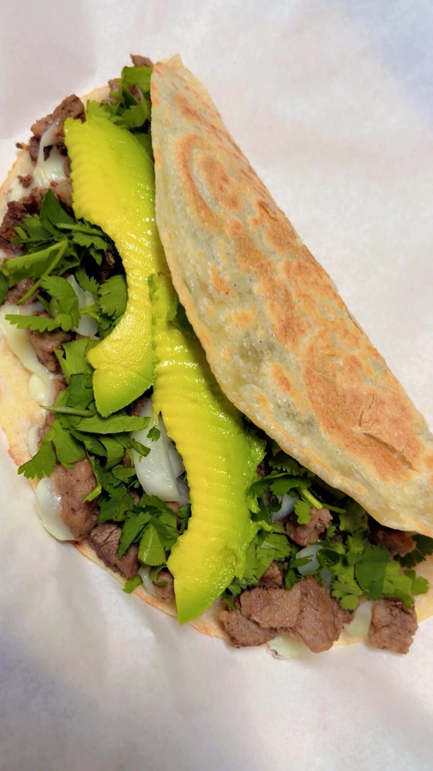 Folded flour tortilla taco with grilled beef, melted cheese, cilantro and avocado slices