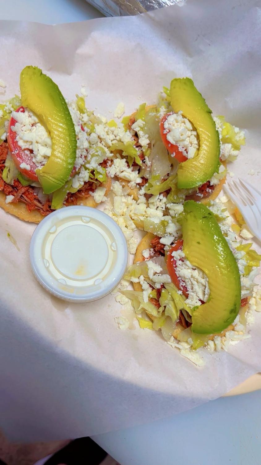 Three sopes topped with shredded meat, lettuce, tomato, queso fresco and avocado